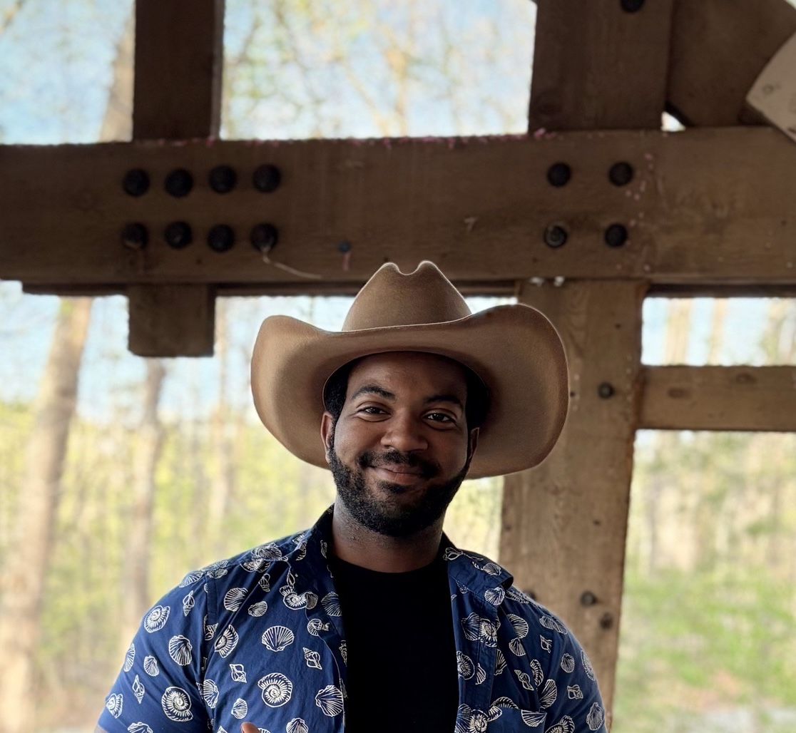 C.J. Fuller smiling in a cowboy hat beneath wooden beams